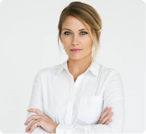 Pewna siebie kobieta o jasnobrązowych włosach, ubrana w białą koszulę, stoi na tle jednolitego tła, z założonymi rękami, o spokojnym i zdecydowanym wyrazie twarzy.