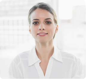 Pewna siebie kobieta w białej bluzce stoi z założonymi rękami na tle jasnego, zamazanego biura, emanując profesjonalizmem i opanowaniem.